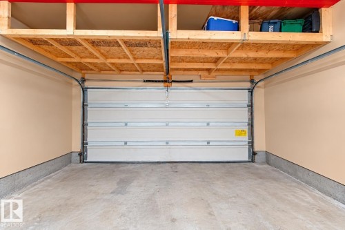 Garage interior featuring concrete flooring, a paneled overhead garage door, and built-in wooden ceiling-mounted storage shelving - 4 1920 Millwoods Rd E Nw, Edmonton, AB 