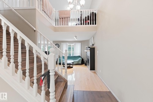 Grand entryway featuring two-story ceilings, a wood-tread staircase with white painted balusters, a suspended multi-bulb chandelier, wood-finish flooring, and a fireplace surround - 4 1920 Millwoods Rd E Nw, Edmonton, AB 