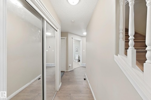 Hallway featuring wood-finish tile flooring, mirrored sliding closet doors, and a white wooden staircase balustrade - 4 1920 Millwoods Rd E Nw, Edmonton, AB 