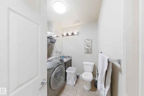 Utility room featuring tile flooring, a vanity with a stone countertop, a three-light wall-mounted fixture, and a white porcelain toilet - 4 1920 Millwoods Rd E Nw, Edmonton, AB 
