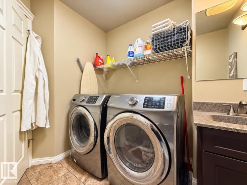Laundry area featuring tile flooring, built-in wire shelving, dark wood-finish cabinetry, a stone-composite countertop, and a vanity sink with a metal faucet - 4 1920 Millwoods Rd E Nw, Edmonton, AB 