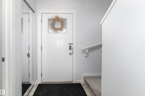 Entryway featuring a paneled door with window, digital lock, mirrored closet doors, and carpeted stairs with a handrail - 6 12815 Cumber Nw, Edmonton, AB 