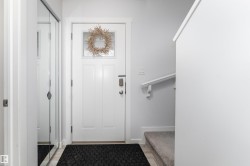 Entryway featuring a paneled door with window, digital lock, mirrored closet doors, and carpeted stairs with a handrail - 