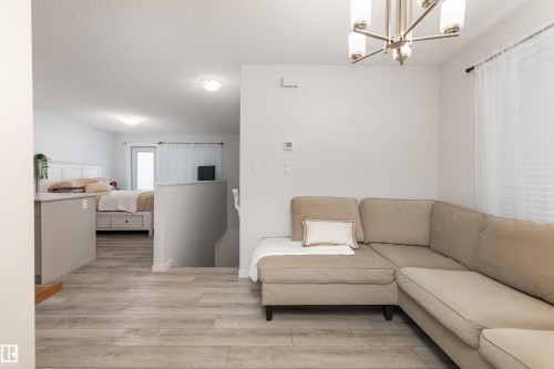 Light wood-finish flooring throughout, modern ceiling light fixture, white walls, and a window with white blinds - 6 12815 Cumber Nw, Edmonton, AB 