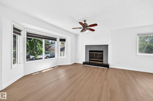 Light wood-finish flooring, a modern fireplace with dark tile surround, a built-in ceiling fan, and a bay window featuring roller blinds - 3924 26A Avenue Nw, Edmonton, AB 
