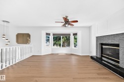 Bay window, wood-finish flooring, contemporary chandelier, stone-clad fireplace, and ceiling fan - 