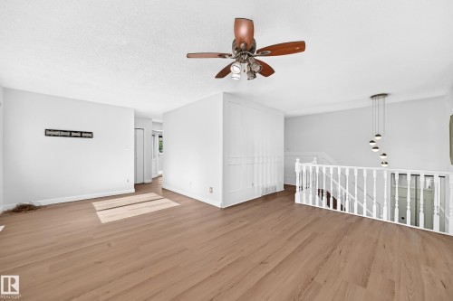 Expansive room featuring wood-finish flooring, a contemporary multi-light pendant fixture, a ceiling fan with integrated lighting, and a white baluster railing - 3924 26A Avenue Nw, Edmonton, AB 
