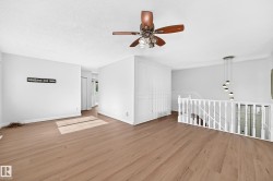 Expansive room featuring wood-finish flooring, a contemporary multi-light pendant fixture, a ceiling fan with integrated lighting, and a white baluster railing - 
