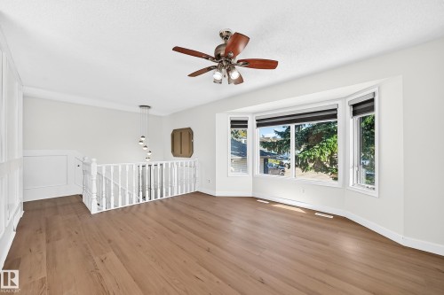 Bay window with multiple panes, wood-finish flooring, white painted walls, ceiling fan with integrated lighting, and a white baluster railing - 3924 26A Avenue Nw, Edmonton, AB 