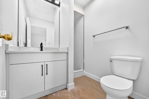White vanity with matte black faucet, glass-enclosed shower, white toilet, and wood-finish flooring - 3924 26A Avenue Nw, Edmonton, AB 