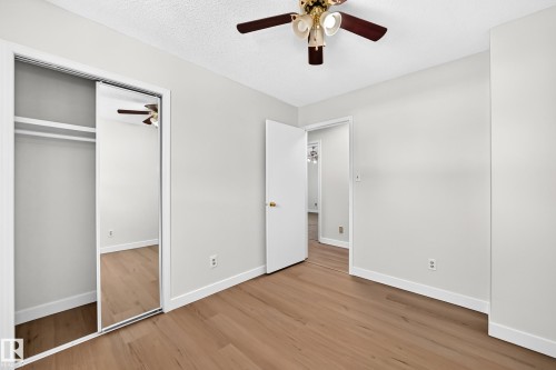Wood-finish flooring, mirrored closet doors, ceiling fan with integrated lighting, and a white interior door - 3924 26A Avenue Nw, Edmonton, AB 