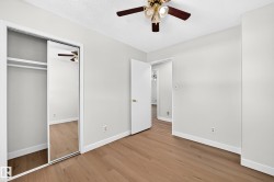 Wood-finish flooring, mirrored closet doors, ceiling fan with integrated lighting, and a white interior door - 