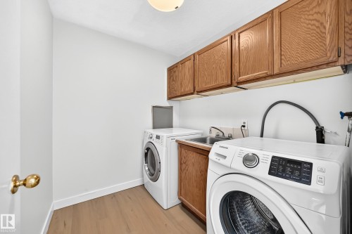 Dedicated laundry area featuring wood-finish flooring, wood cabinetry, and an integrated utility sink - 3924 26A Avenue Nw, Edmonton, AB 