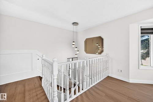 Wood-finish flooring, white spindle railing, modern pendant light fixture, wall-mounted mirror, and a window with exterior visibility - 3924 26A Avenue Nw, Edmonton, AB 