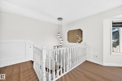 Wood-finish flooring, white spindle railing, modern pendant light fixture, wall-mounted mirror, and a window with exterior visibility - 