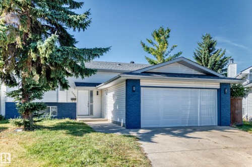 Front exterior featuring white siding, a contrasting dark blue lower facade, an attached garage with a concrete driveway, a front entrance with a white door, and a mature tree - 3924 26A Avenue Nw, Edmonton, AB 