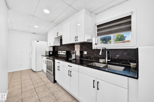 White cabinetry with black hardware, black countertops, and a black and white patterned backsplash - 3924 26A Avenue Nw, Edmonton, AB 
