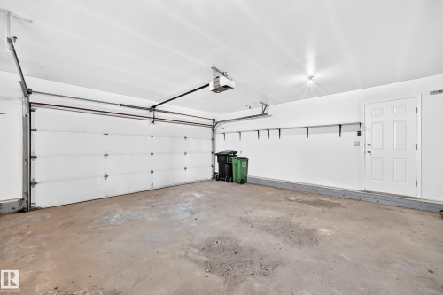 Attached garage with a white sectional door, automatic garage door opener, interior access door, and wall-mounted shelving brackets - 3924 26A Avenue Nw, Edmonton, AB 