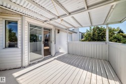 Outdoor deck featuring white painted wood plank flooring, a white corrugated metal roof, a white wood railing, and vinyl siding - 