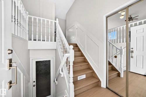 Hardwood stairs with white balusters, wainscoting detailing, and a mirrored closet door - 3924 26A Avenue Nw, Edmonton, AB 