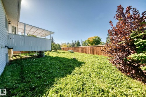 White siding, covered elevated deck, wood fence, and mature trees - 3924 26A Avenue Nw, Edmonton, AB 