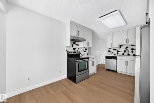 Contemporary kitchen featuring white cabinetry, a graphic black and white backsplash, stainless steel appliances, and wood-finish flooring - 3924 26A Avenue Nw, Edmonton, AB 