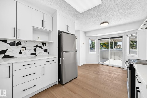 White cabinetry with matte black hardware, geometric tile backsplash, light wood-finish flooring, and a sliding glass door - 3924 26A Avenue Nw, Edmonton, AB 