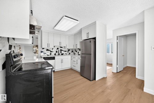 Kitchen featuring white cabinetry, wood-finish flooring, stainless steel refrigerator, white countertops, and a distinct geometric backsplash - 3924 26A Avenue Nw, Edmonton, AB 