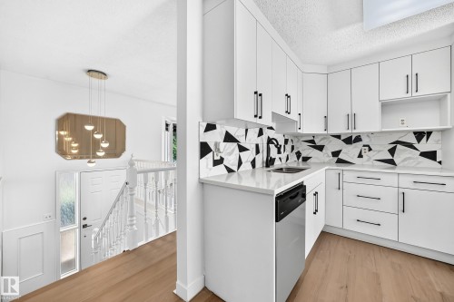 Updated kitchen featuring white cabinetry, black hardware, geometric backsplash, and light wood-finish flooring - 3924 26A Avenue Nw, Edmonton, AB 