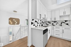 Updated kitchen featuring white cabinetry, black hardware, geometric backsplash, and light wood-finish flooring - 