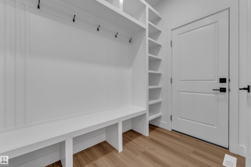 Built-in mudroom bench with coat hooks, open shelving, paneled door, and wood-finish flooring - 3604 44 Avenue, Beaumont, AB 