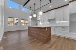 Two-story ceiling, large upper windows, wood-finish flooring, kitchen island with solid surface countertop, and white shaker cabinetry - 