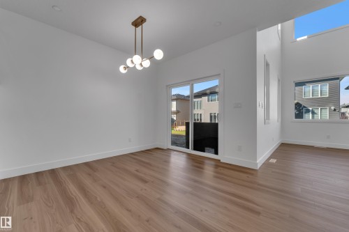 Wood-finish flooring with a modern ceiling light fixture, featuring multiple windows and a sliding glass door - 3604 44 Avenue, Beaumont, AB 