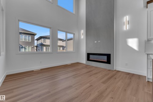 Two-story ceiling, multiple large windows, wood-finish flooring, linear electric fireplace, and built-in wall sconces - 3604 44 Avenue, Beaumont, AB 