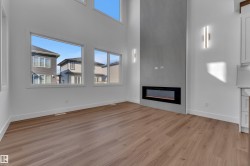 Two-story ceiling, multiple large windows, wood-finish flooring, linear electric fireplace, and built-in wall sconces - 