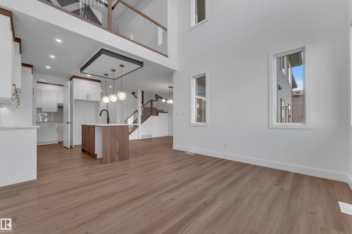 Wood-finish flooring throughout, kitchen island with built-in sink, white cabinetry with gold hardware, modern pendant lighting, and a multi-level staircase with glass railing - 3604 44 Avenue, Beaumont, AB 