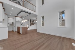 Wood-finish flooring throughout, kitchen island with built-in sink, white cabinetry with gold hardware, modern pendant lighting, and a multi-level staircase with glass railing - 