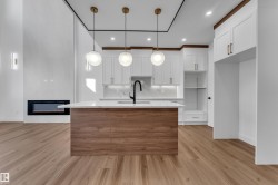 Open-concept living area with wood-finish flooring, a contemporary linear fireplace, and a kitchen featuring white cabinetry and a central island with a waterfall countertop - 