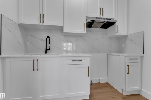 White cabinetry with gold-tone hardware, white marble-patterned backsplash, light-toned wood-finish flooring, and a matte black faucet - 3604 44 Avenue, Beaumont, AB 