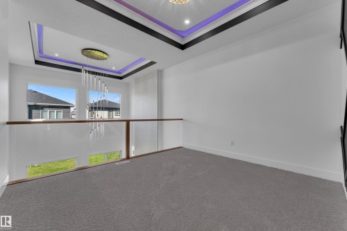 Recessed lighting, tray ceiling with accent lighting, contemporary chandelier, glass railing with wood-finish top, and carpeted flooring - 3604 44 Avenue, Beaumont, AB 