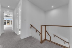 Wall-to-wall patterned carpeting, recessed ceiling lighting, a clear glass stair railing with wood-finish top and bottom rails, and a wood-finish handrail - 