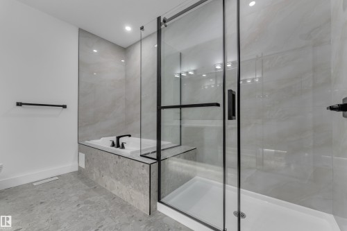 Walk-in shower with clear glass enclosure and black frame, featuring a built-in tub with matte black fixtures - 3604 44 Avenue, Beaumont, AB 