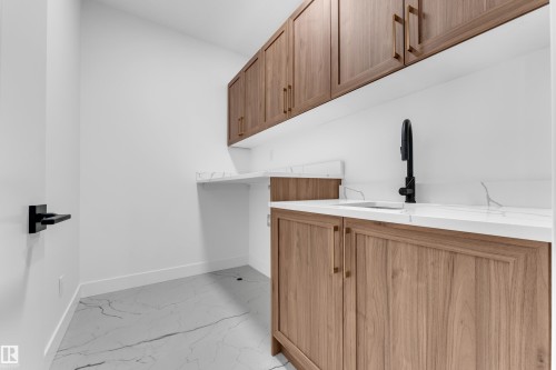 Wood-finish cabinetry with gold-tone hardware, white countertops with veining, and a matte black gooseneck faucet - 3604 44 Avenue, Beaumont, AB 