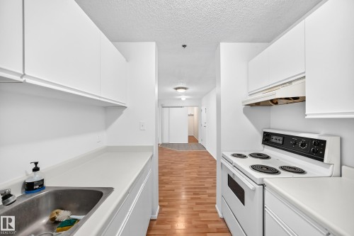 Kitchen featuring white cabinetry, solid surface countertops, a stainless steel sink, and a white electric range - #212 11218 80 St Nw, Edmonton, AB 