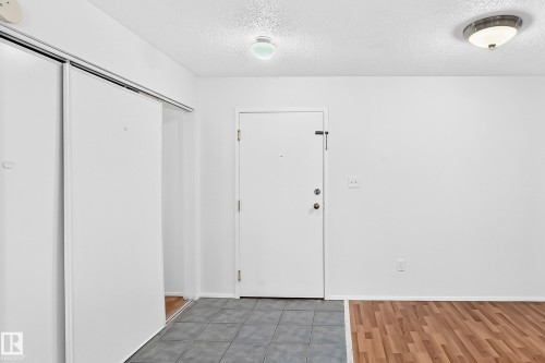 Entryway with gray tile flooring, adjacent wood-finish flooring, and white walls - #212 11218 80 St Nw, Edmonton, AB 