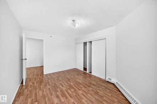 Wood-finish flooring, white walls, built-in sliding closet, ceiling-mounted light fixture, and baseboard heating unit - #212 11218 80 St Nw, Edmonton, AB 