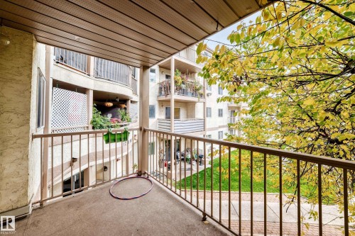 Private balcony with a textured concrete floor and metal railing, overlooking a landscaped grassy area - #212 11218 80 St Nw, Edmonton, AB 
