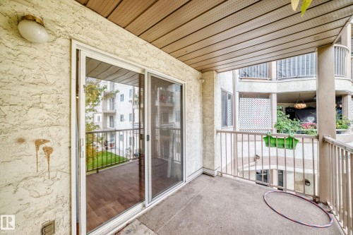Concrete balcony with metal railings, featuring a sliding glass door and an attached exterior light fixture - #212 11218 80 St Nw, Edmonton, AB 