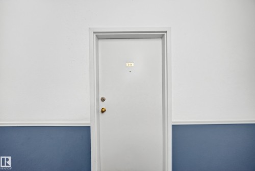 White door with brass hardware and a gold-tone number plaque - #212 11218 80 St Nw, Edmonton, AB 