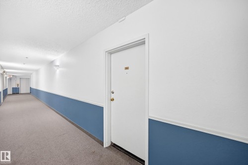 Long hallway featuring carpeted flooring and wall-mounted lighting - #212 11218 80 St Nw, Edmonton, AB 